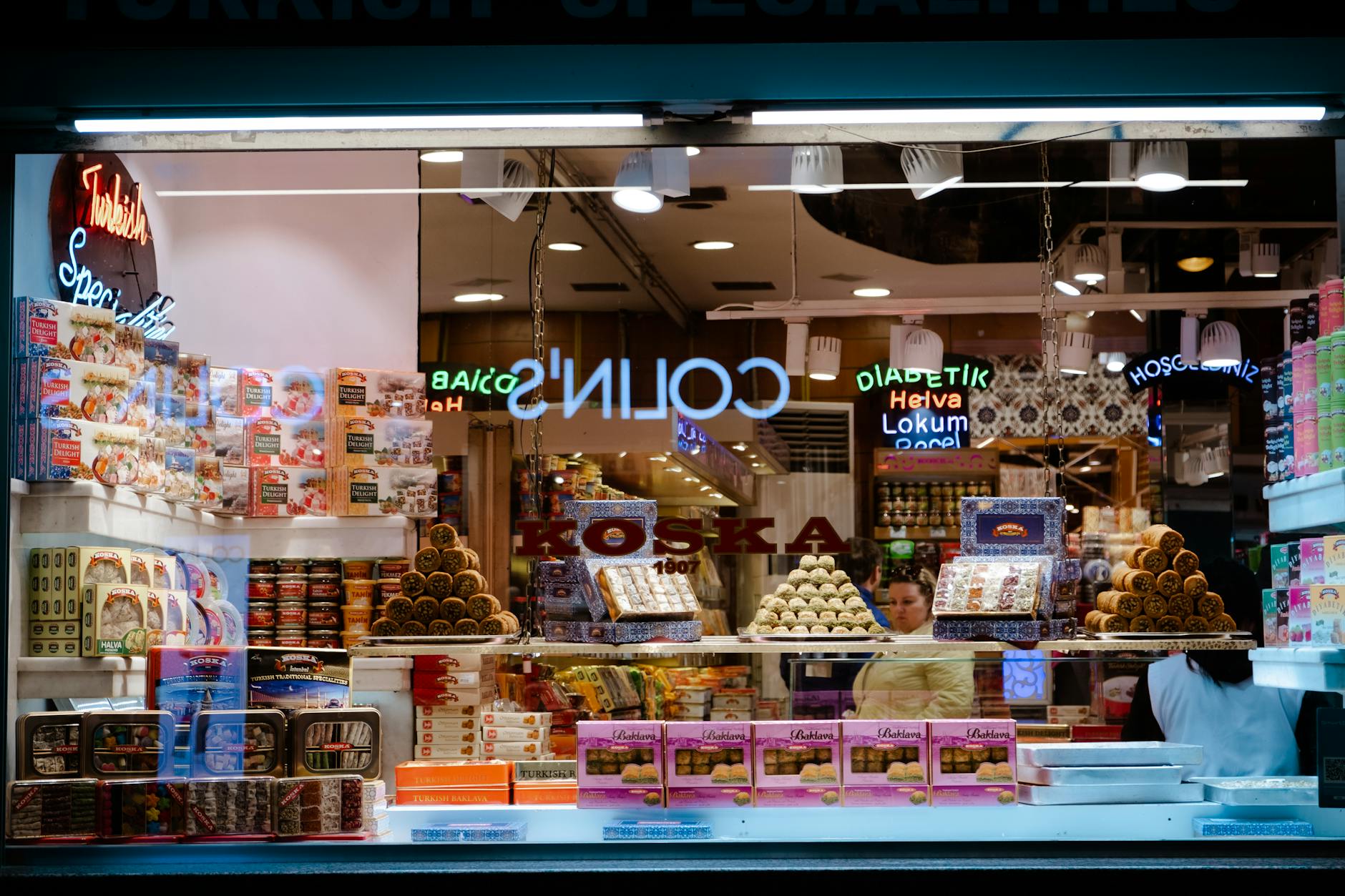 Colorful display of Turkish sweets in a shop window at night, featuring neon lights and variety of products.