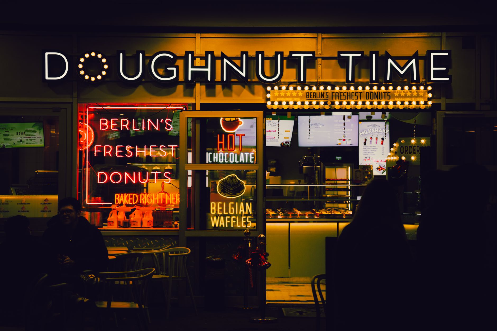A vibrant Berlin doughnut shopfront at night with neon lights and cozy ambiance.