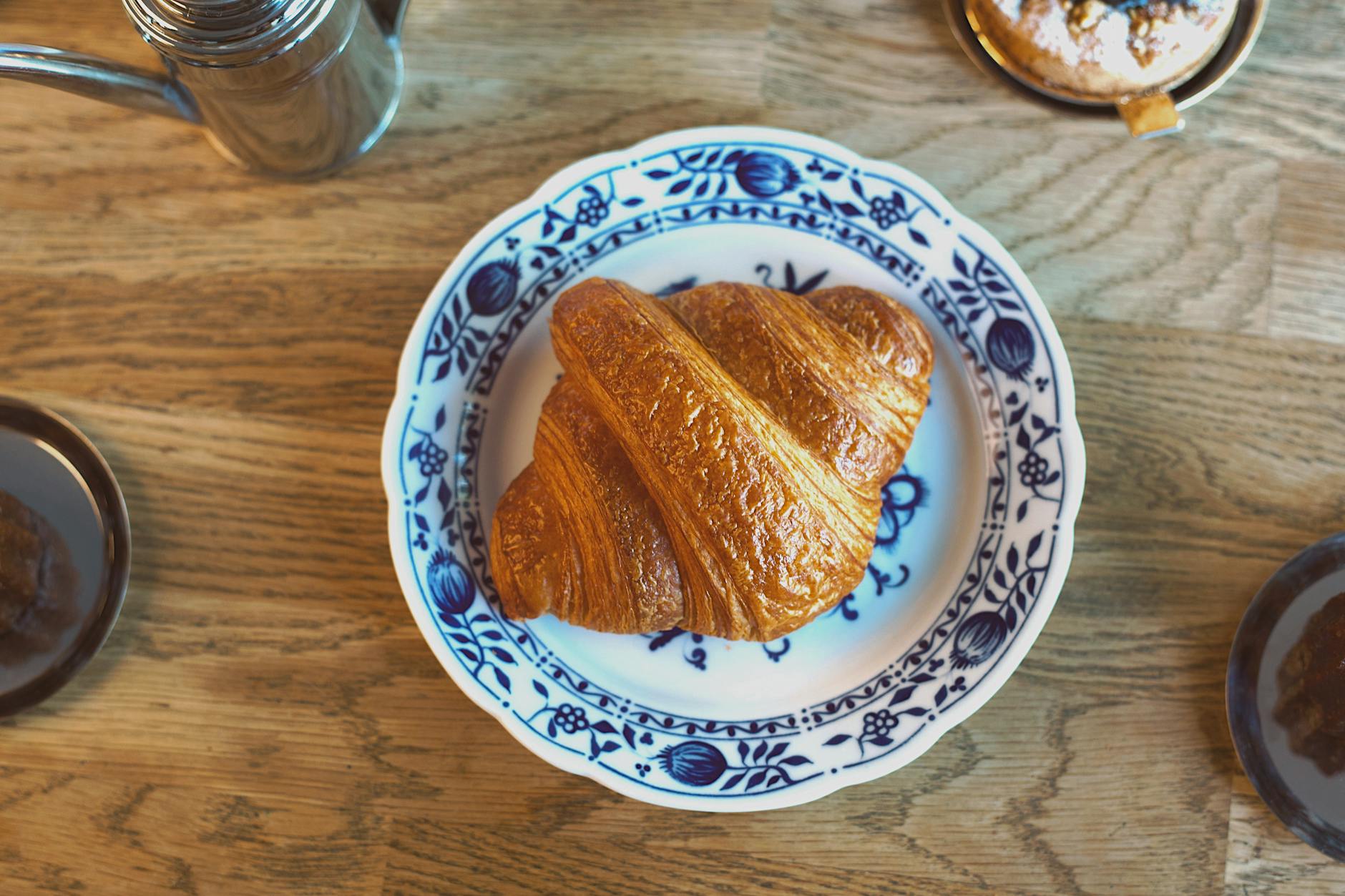Golden brown croissant on ornate plate in cozy Berlin cafe. Perfect brunch scene.