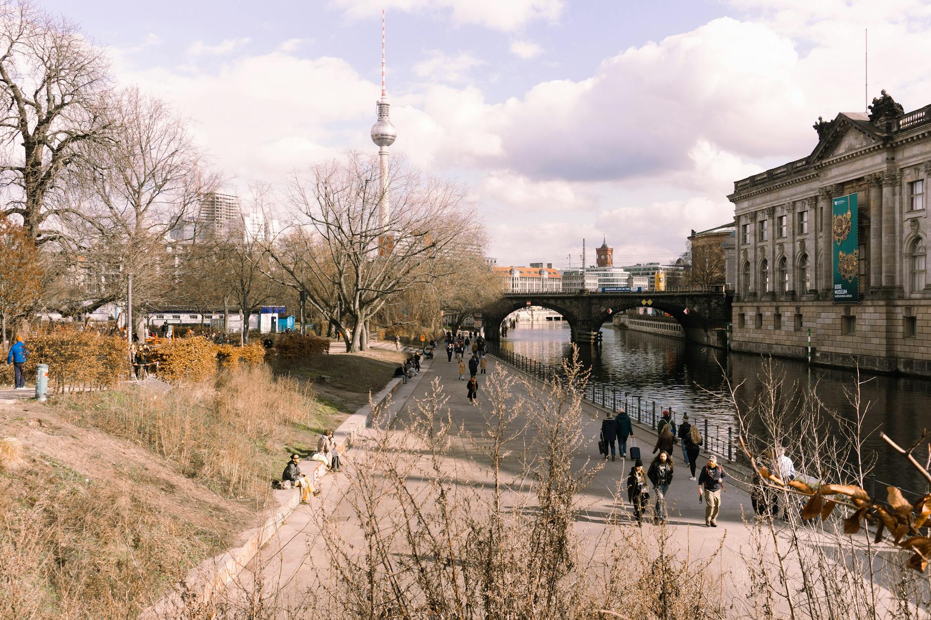 Scenic view of Berlin with the TV Tower, river, and people strolling. Perfect blend of nature and city.
