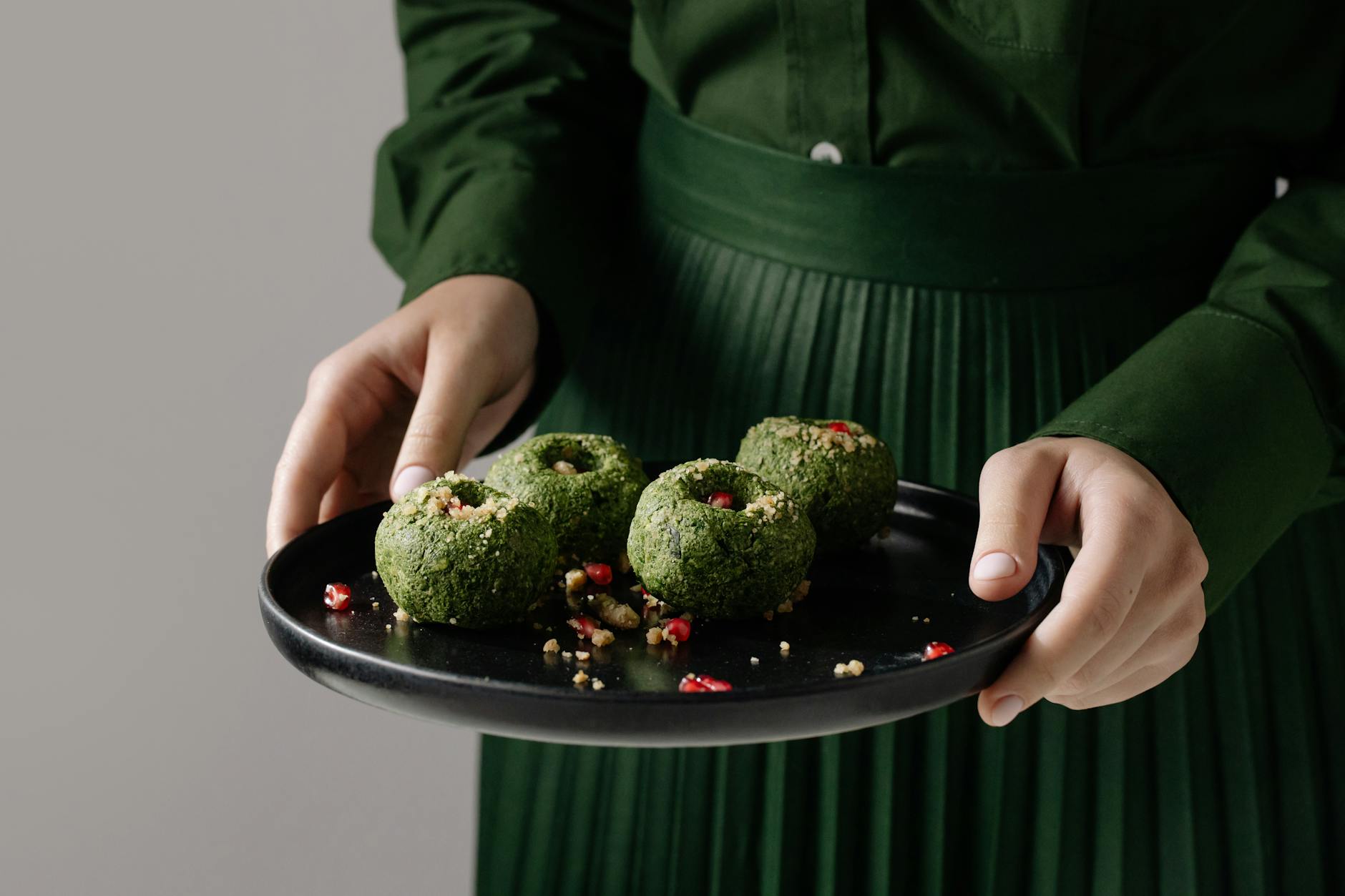 Delicious Georgian spinach pkhali on a black plate, held by a person in green attire.