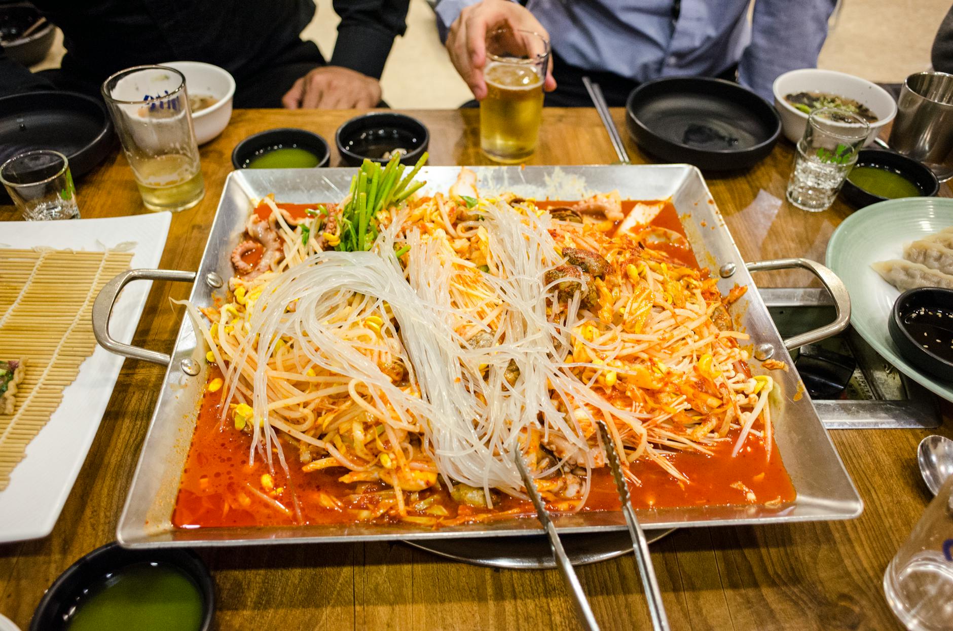 A vibrant tabletop spread featuring spicy Korean hot pot with rice noodles and various side dishes.