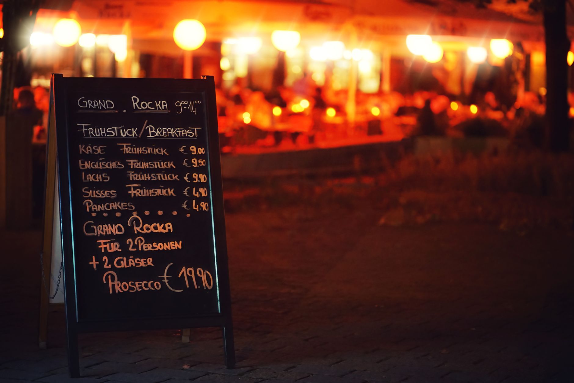 Chalkboard menu outside a Berlin restaurant, illuminated at night, offering breakfast options.